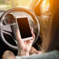 woman holding her cell phone instead of the steering wheel